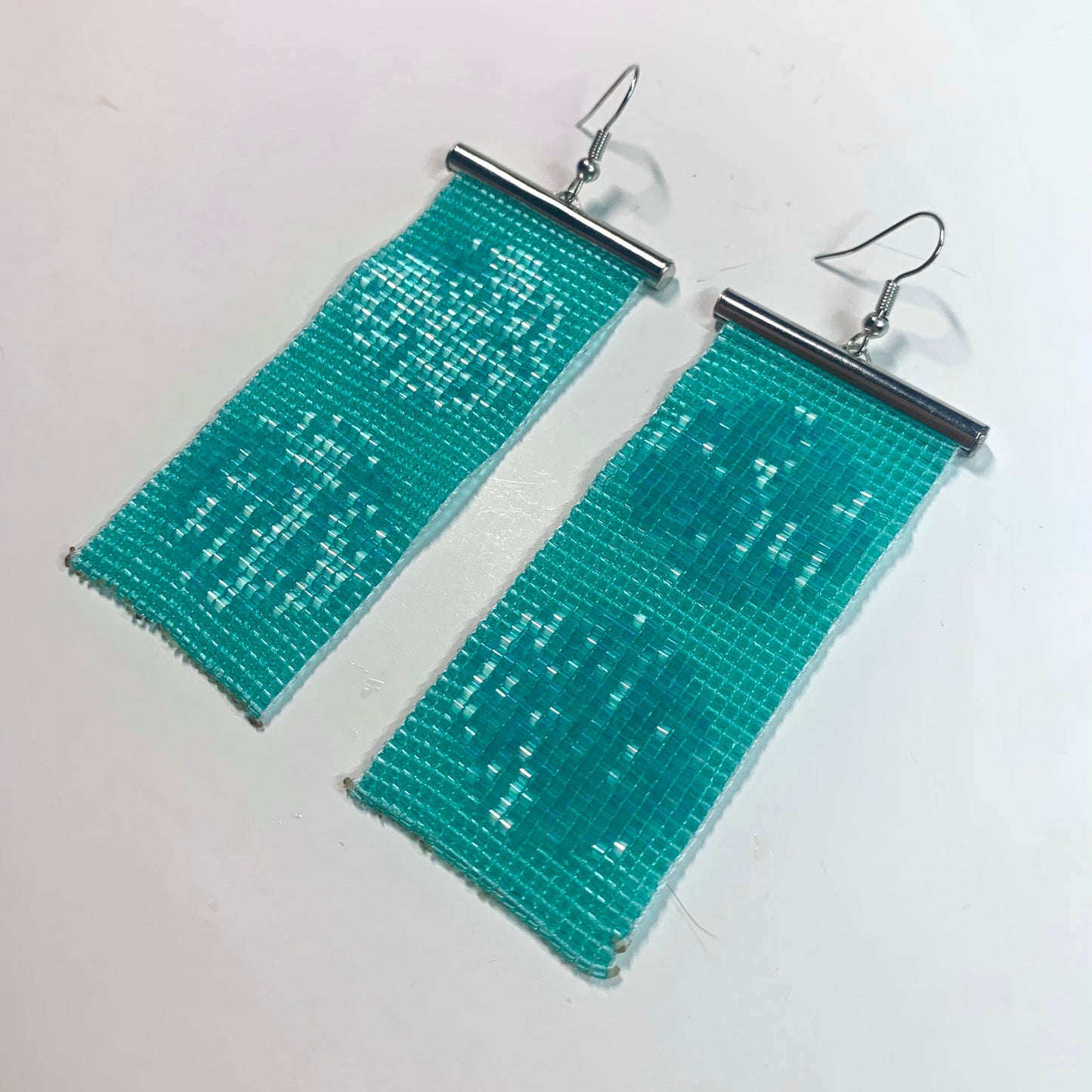 Teal rectangular beaded earrings on a white background