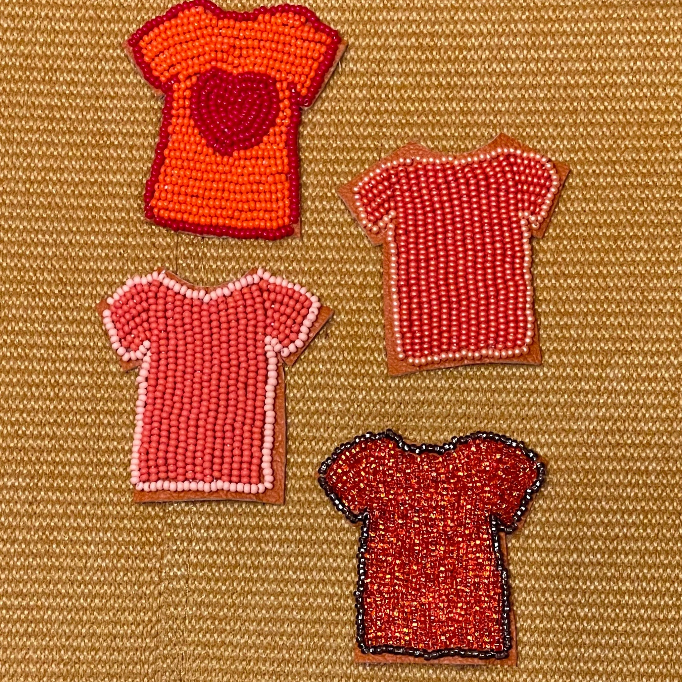 Four beaded t-shirt patches in red, orange, and pink, arranged on a textured tan woven background.