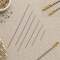 John Bead Gold Eye beading needles in multiple sizes arranged on a linen background