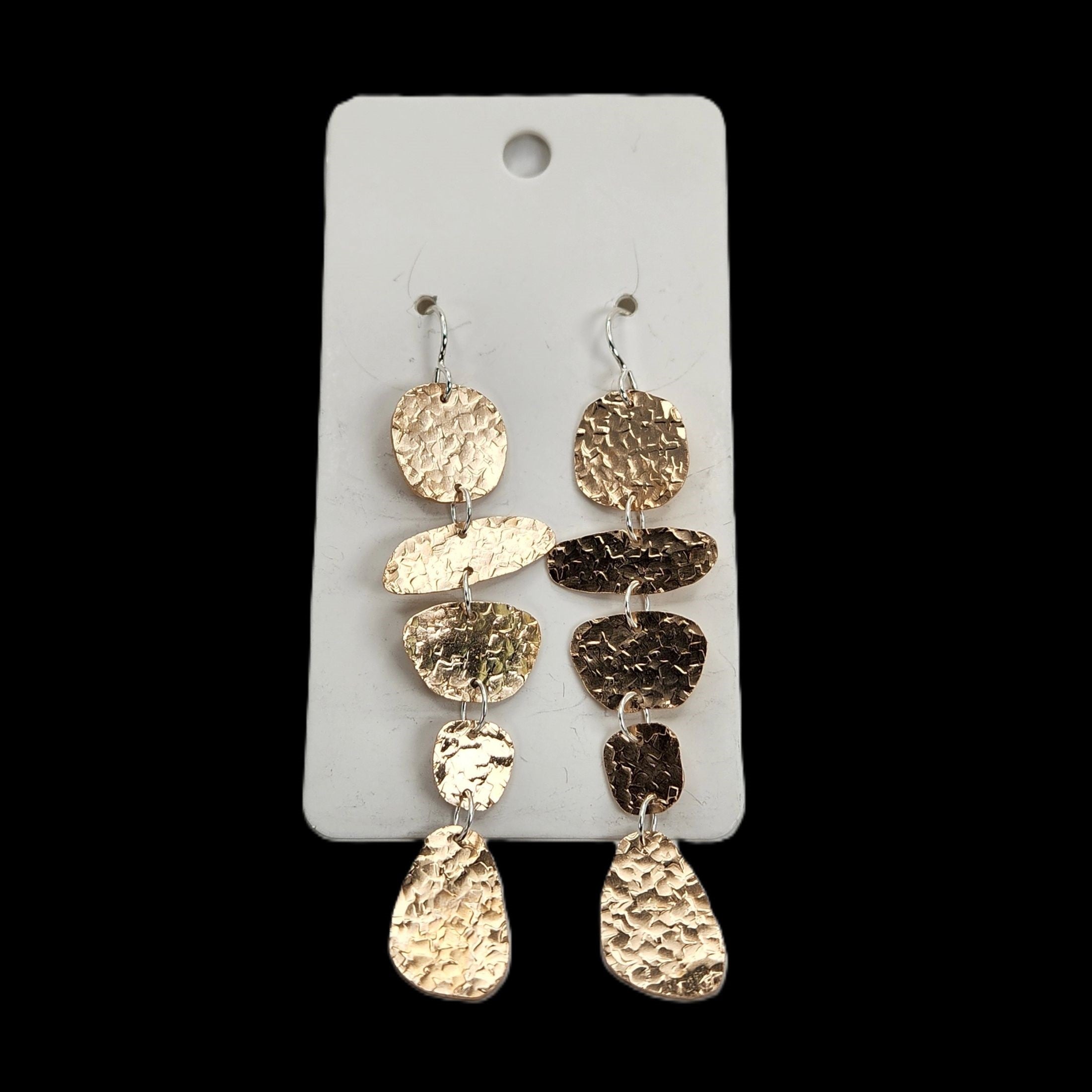 Pair of bronze dangling earrings on a white card against a black background